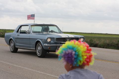 Spectator in a rainbow wig watching a classic Mustang